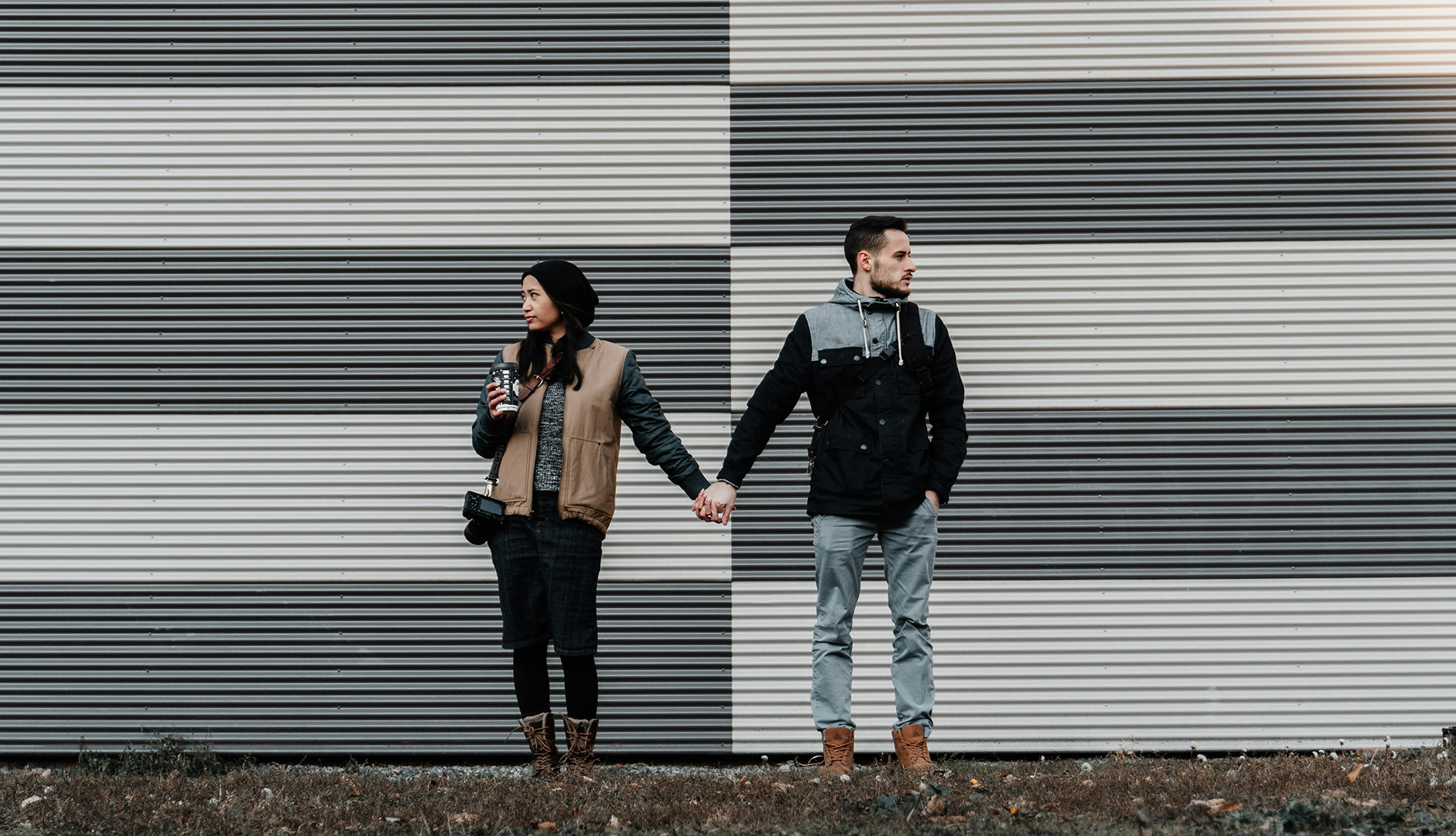 Two people standing next to each other holding hands. They are both looking away from each other, and appear disconnected. 