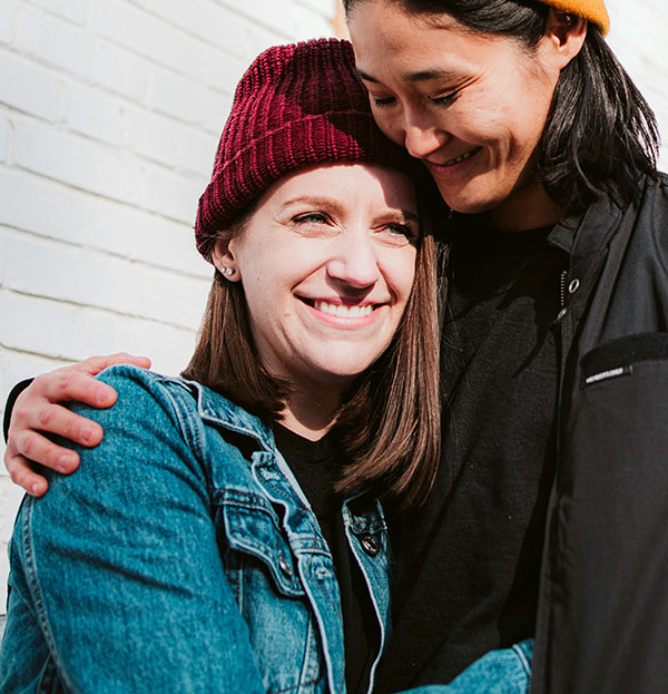 Two women hugging each other and smiling. One woman has her arm wrapped around the other, pulling the other into her chest