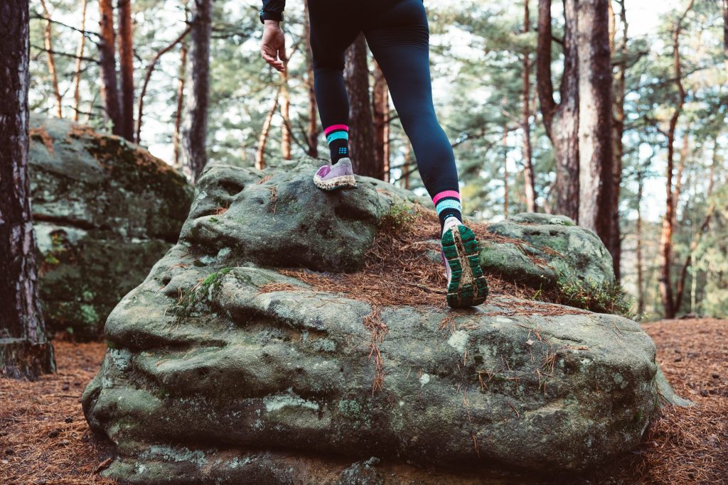 Photo of a woman trail running over a boulder in a forest, symbolizing the flight response and allowing the body to do what it needs in order to take care of itself