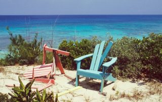 A photo of two colorful, broken Adirondack chairs sitting on the edge of a cliff in the sunshine.